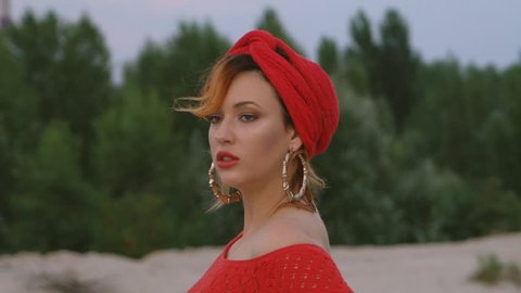 close-up portrait. lovely red-haired woman on the beach. woman 25 years of sexually dancing in the sand. eastern motif. long red dress, red oriental turban, large gold earrings.
