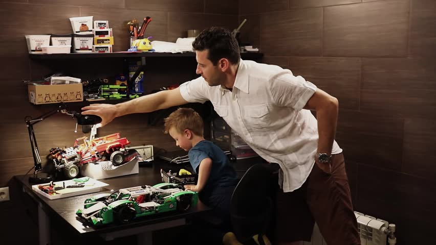 Son and father adjusts lamp above table with cars models in garage. Slow motion