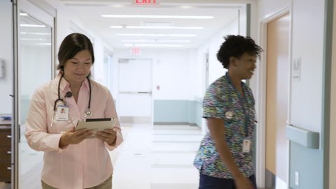 Handheld shot of confident doctor with digital tablet instructing nurse while walking in corridor at hospital