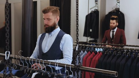 Bearded stylish man in elegant suit chooses clothes in the tailor salon.