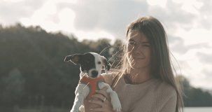 Portrait of beautiful young woman playing with dog jack russell terrier on the lake shore. A girl whirl in dance with a cute puppy. 4K video shooting