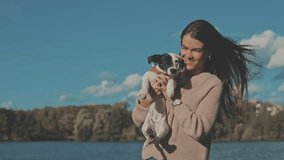 Portrait of beautiful young woman playing with dog jack russell terrier on the lake shore. A girl whirl in dance with a cute puppy. Slow motion video shooting