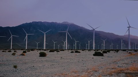 Windmills spinning at sunset in a dry desert with mountain range in background. TILT start into static composition.