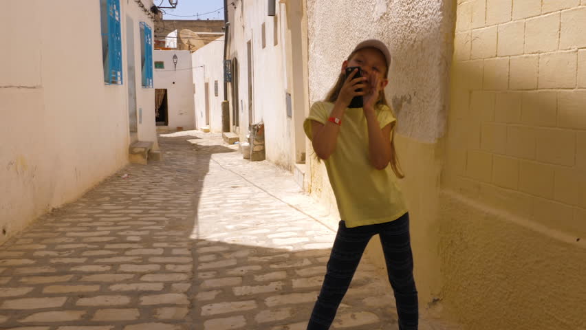 Funny girl singing and dancing with phone on narrow street in old town