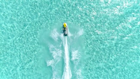 Aerial - Epic shot of a jet ski racing on a crystal clear water. Adult male enjoying summer vacation in Bora Bora speeding on a jet ski 