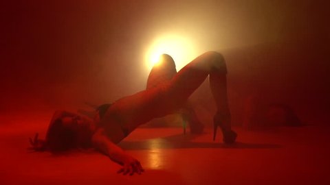 Two women in stockings are dancing a strip dance on the floor in the smoke, bit slow motion