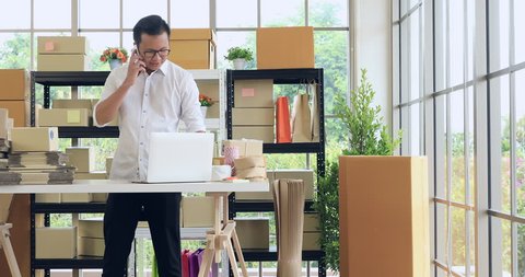 Young and handsome Asian man working in home office in online business, looking to laptop computer and fasten parcel with rope prepare for deliver to customer.