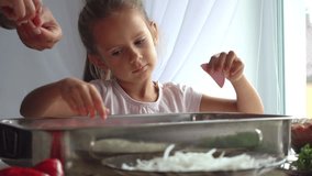 Portrait of a little girl who helps her mother in the kitchen. Daughter helps mom in pizza making 4k video. The child learns to cook food.