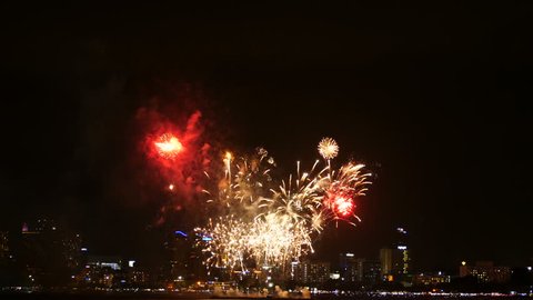 4K footage of real fireworks festival in the sky for celebration at night with city view at background and boat floating on the sea at foreground at coast side