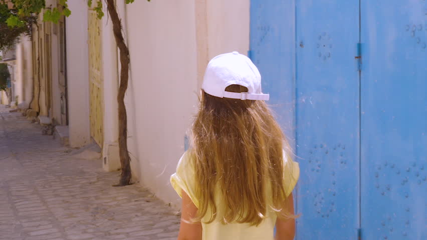 Girl teenager inviting to follow her on narrow street in old town back view