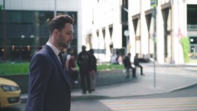 Side view of handsome young businessman in dark suit walking in a summer street. Concept of business and life success. Tracking slow motion low medium shot