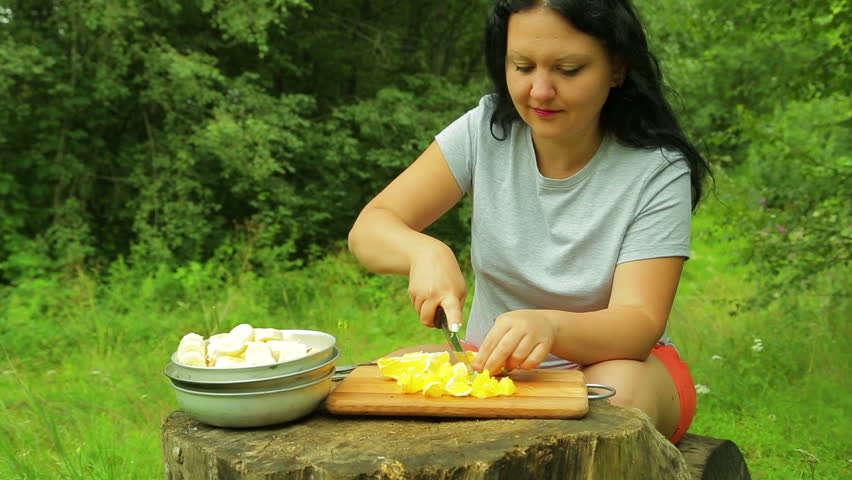 Woman slicing fresh orange fruit with slices on a wooden salad board for a picnic.