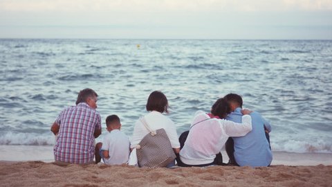 Big friendly family sitting on beach and admiring sea view
