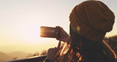 Young Woman Taking Pictures of Sunlit Fall Mountain Landscape form the Top. SLOW MOTION. Hiker Girl is Taking photos with smartphone of autumn hills landscape at sunset, Lens Flare. Video stock