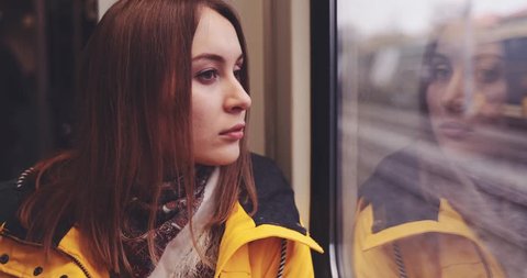 Sad Young Woman Looking Out of a Train Window. SLOW MOTION 4K. Tired, depressed girl thinking of something seating near the window in city train during her daily commute.