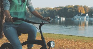 Beautiful summertime mood shot of young woman or girl riding bicycle through promenade, in stylish outift, pedalling next to trees in sun light, 4K video shooting by handheld gimbal