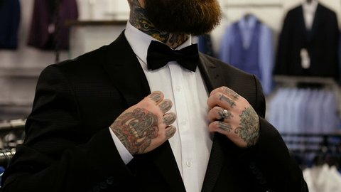 Close view of an elegantly dressed bearded man who trying on a suit while standing in a men's clothing store.