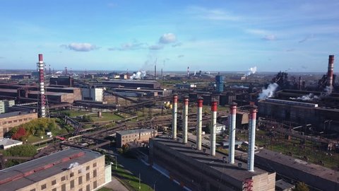 Drone panning of industrial park, many smoke stack pipes of steel plant, technogenic landscape with autumn bright trees, concept of pollution, air emissions from manufacturing sector, industrial city