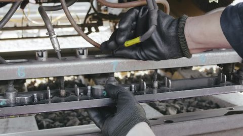 Male hands in black protective gloves repair the train, standing on rails. Maintenance service of railway trains