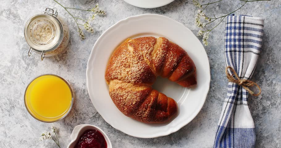 Top view of served baked croissant on plate with cup of coffee and glass of juice on table with jam in bowl