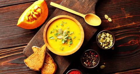 From above view of yellow fresh pumpkin soup sprinkled with herb served with spoon and bread on cutting board on wooden background Arkivvideo