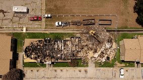 In this aerial clip a drone descends and films a tragic scene. An excavator is demolishing a completely burned down house.