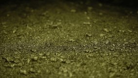 This stock video features a close-up shot of pieces of gold falling onto a gold-flecked surface. The clip was taken while on an isolated black background. 