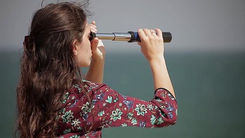 Brunette young woman watching horizon through spyglass profile
