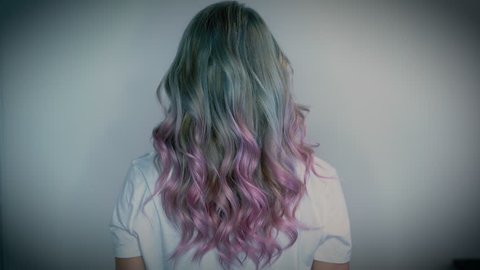 Girl with long platinum, blue and pink unicorn hair style from the back gently shaking her head.