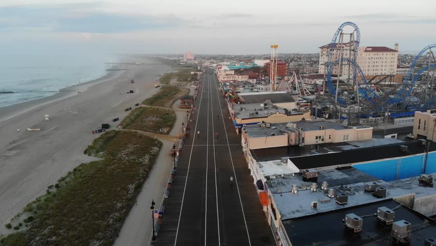 Aerial Drone Views Flying Over Ocean City New Jersey Boardwalk Shops and Beach Hotels, City Skyline and Atlantic Ocean Coastline With Green Dunes and Clear Skies on Horizon 