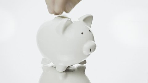 Filling a piggybank (a porcelain container for money) with Euro coins. White background. A piggy bank is a small bank, having the shape of a pig, provided with a slot at the top to receive coins.
