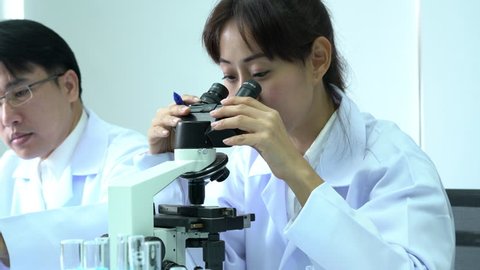 Scientist female is looking through microscope with colleagues working in modern laboratory or medical center together. Concept of science, testing development and lab industry.