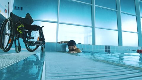 Disabled man gets out of the swimming pool. Side view