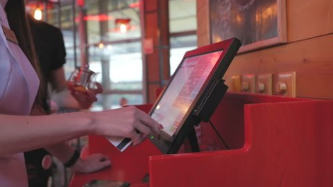 The waitress makes an order for the kitchen using a touch computer or POS system in the restaurant, pressing her fingers on the monitor screen.
