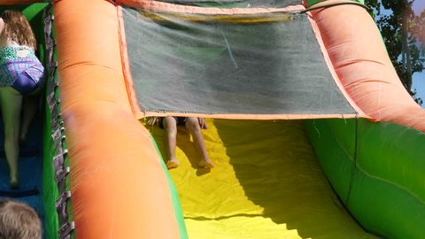 A slow motion shot of kids playing on a blow up bouce house water slide on a hot summer day