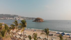 Aerial clip approaching a rock in the pacific ocean, in front of the coast of Acapulco.