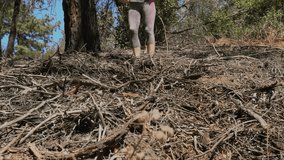 This video shows a close up view of a fit woman running down a hill covered in branches towards the camera.