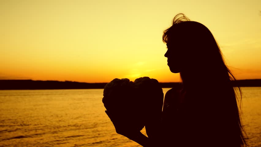 eautiful girl holding heart in sunset. close up. silhouette of girl holds heart at beautiful sunset against sea.