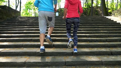 Active young couple jogging up the stairs in the park, super slow motion
