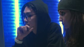 Cute young girl and asian guy hacker create a new computer virus sitting in the office with dark lighting. Concept of programming and hacking. 4k