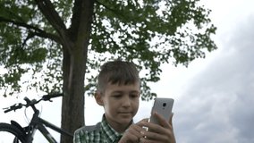 happy boy uses a phone in the park under the tree