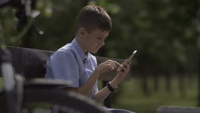 biker boy in hat sitting on bench in park after riding bicycle uses phone