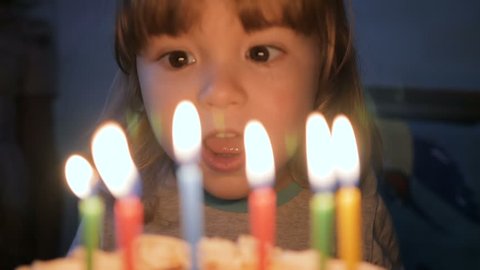 Little boy blows out candles on birthday cake at party. Closeup. Slow motion.
