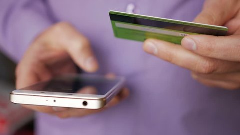 Businessman in a purple shirt making online payment with credit card and smartphone, online shopping, lifestyle technology. Man enters the bank card number into the smart phone. Closeup. Close up.
