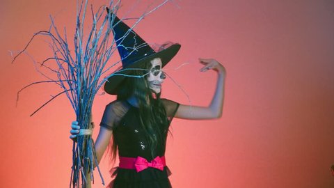 Halloween, girl with makeup skeleton on half face, dressed as a witch, posing and dancing on a red background. 4k, slow motion