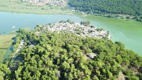 Aerial drone bird's eye view video of iconic vegetated small inhabited island in lake of Ioannina surrounded by mountains of Pindus, Epirus, Greece