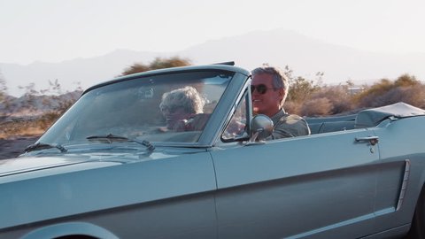 Senior white couple driving classic convertible on highway