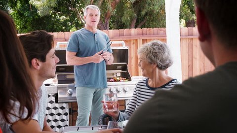 Family at a table outdoors turn to dad standing by barbecue