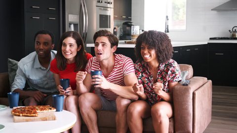 Four young adult friends watching sports on TV celebrating