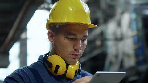 Close up face of hardworking man in bump cap using tablet computer application when working in industrial building